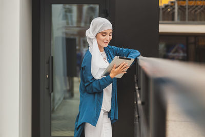 Portrait of young woman standing against window