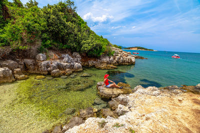 Rear view of man standing on rock by sea against sky