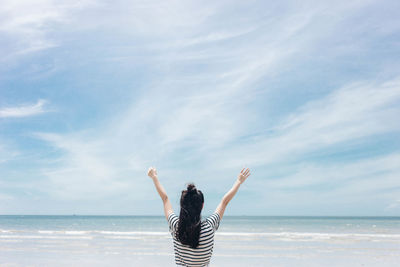 Rear view of woman with arms raised standing against sky at beach