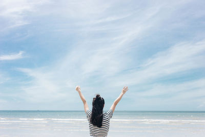 Rear view of woman standing at beach against sky