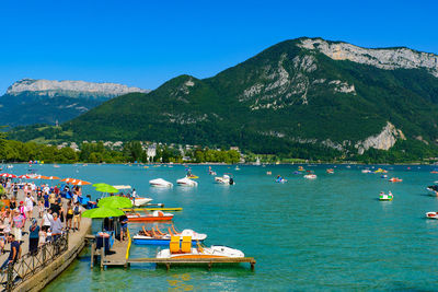 People on boats in sea against clear blue sky