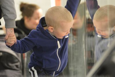 Boy holding hand of parent while looking at reflection