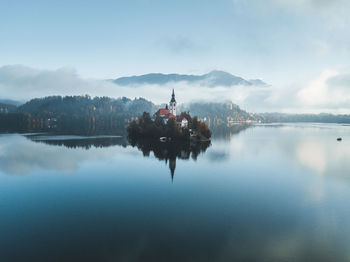 Scenic view of lake by building against sky. fantastic sunrise with mist in bled, slovenia