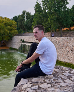 Portrait of young man sitting on retaining wall