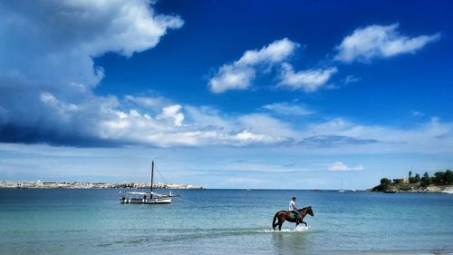 Side view of man riding horse in sea against cloudy sky