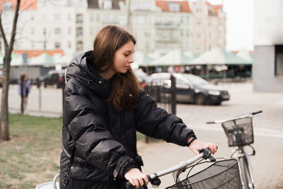 Smiling young woman with bicycle standing on footpath