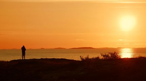 Silhouette person standing on beach against sky during sunset