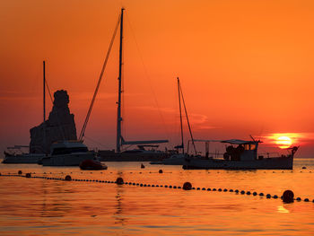 Silhouette sailboats on sea against orange sky