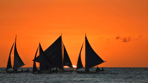 Sailboats sailing in sea against orange sky