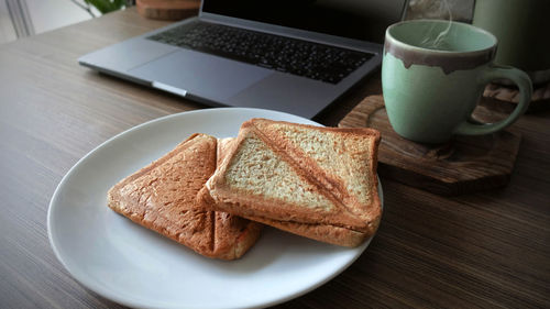 Closeup bun with coffee cup and laptop on wooden table, morning time, empty space for text