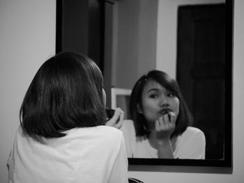 Rear view of woman applying lipstick while reflecting on mirror