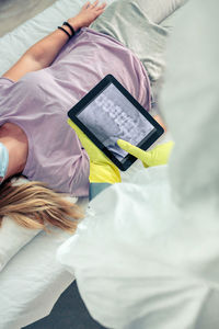 Top view of unrecognizable female doctor in protective suit examining x-ray of patient on tablet