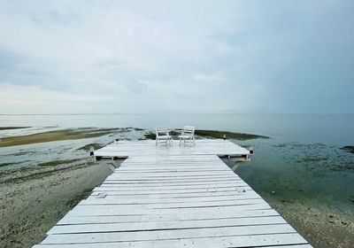 Two white chairs on a foot bridge ieading to  blue sea against cloudy sky