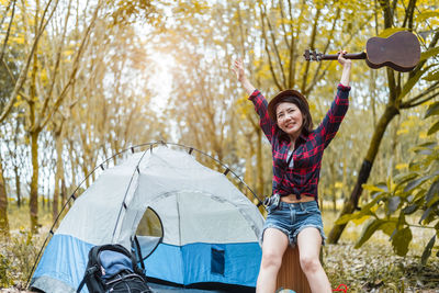 Young woman sitting with ukulele at campsite in forest