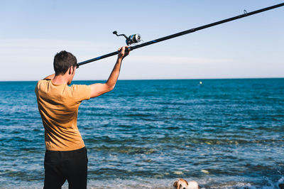 Rear view of man standing in sea against sky