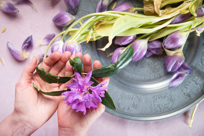 A piece of raspberry layer cake in a woman's hand lilac spring tulips on a plate