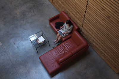 High angle view of businesswoman using laptop computer while sitting on couch in waiting room