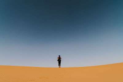 Woman standing on sand dune in desert against clear sky