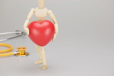 Close-up of wooden figurine carrying heart shape against gray background