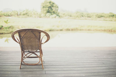 Empty chair on table by lake against sky