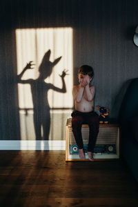 Portrait of shirtless boy sitting against shadow on wall