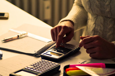 Midsection of woman using calculator while sitting at desk