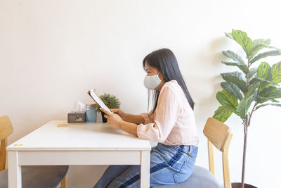 Woman sitting on chair against wall