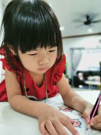 A young girl in red dress coloring on a paper
