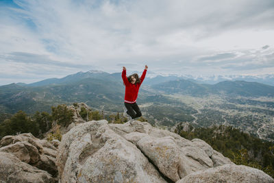 Girl jumping with arms raised on mountain against sky