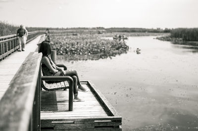 Man sitting on jetty by pier on lake