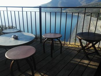 Empty chairs and table by sea against sky