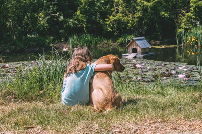 Friendship of animals and children, people.girl sits on the bank of a pond and hugs a labrador