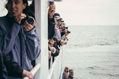 People photographing at sea shore against sky