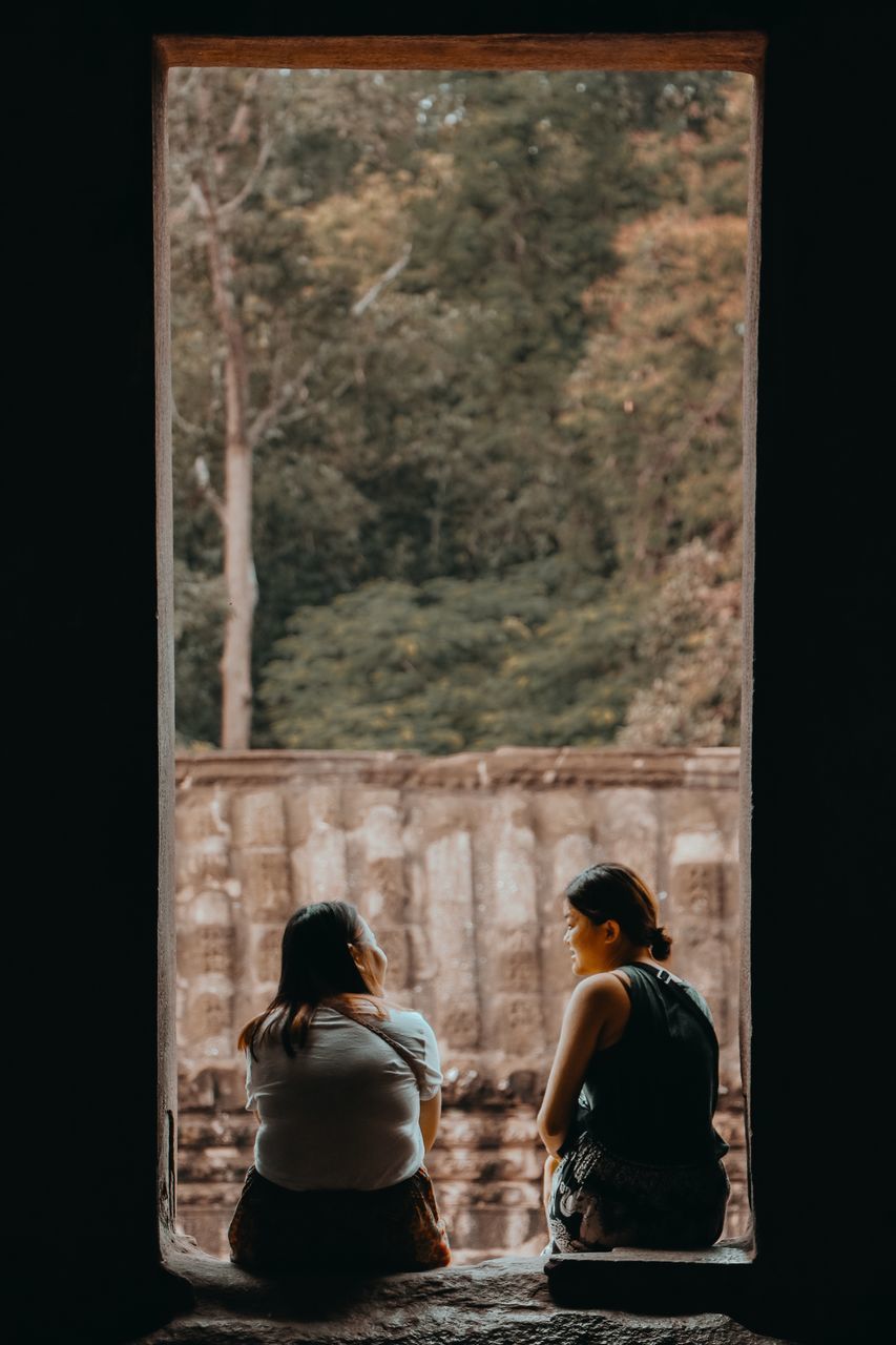 REAR VIEW OF PEOPLE SITTING ON WINDOW