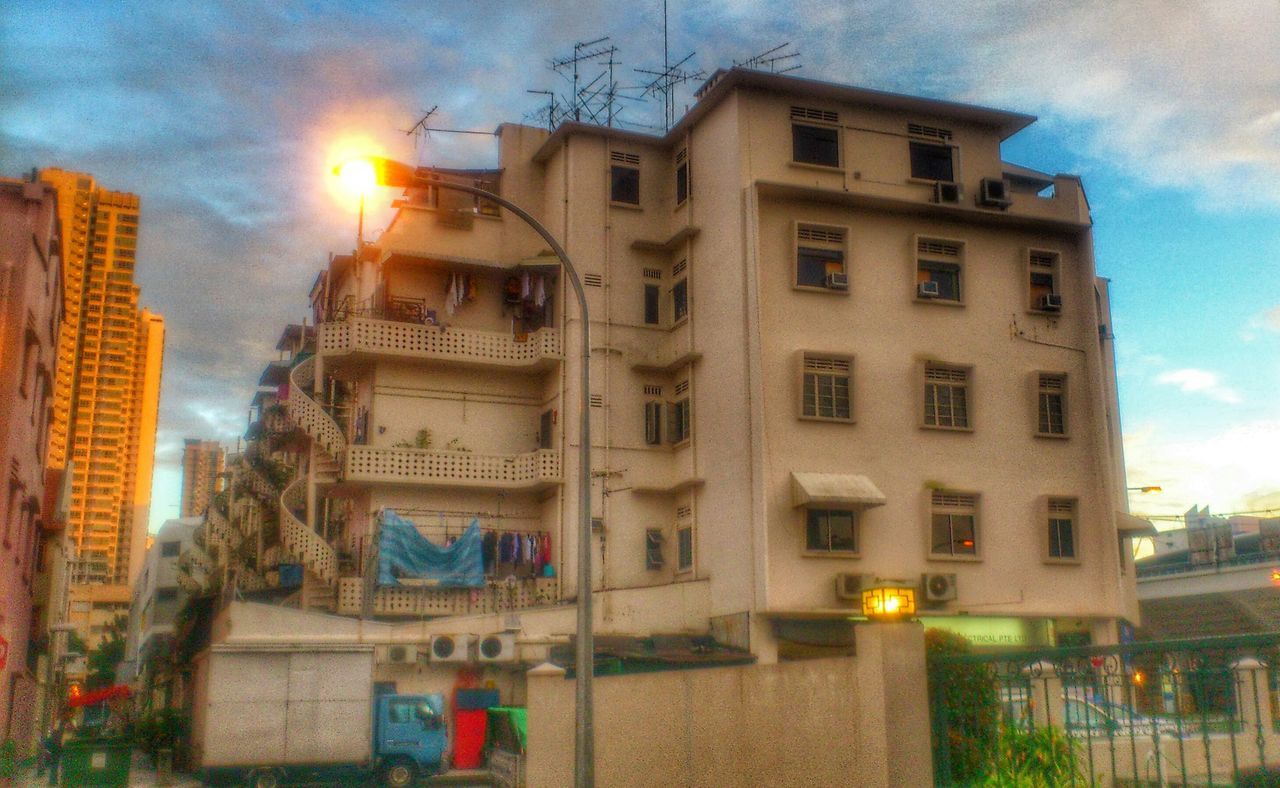 architecture, building exterior, built structure, sky, city, cloud - sky, building, residential building, sunset, window, sun, low angle view, street, sunlight, residential structure, cloud, street light, lens flare, city life, car