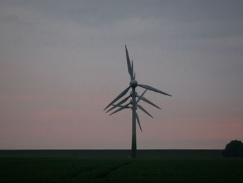 Wind turbines on field against sky during sunset