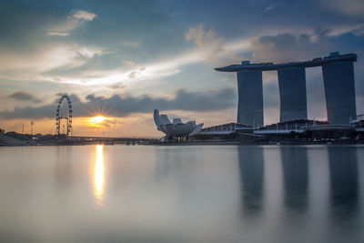 Artscience museum with marina bay sands reflecting in water against sky during sunset