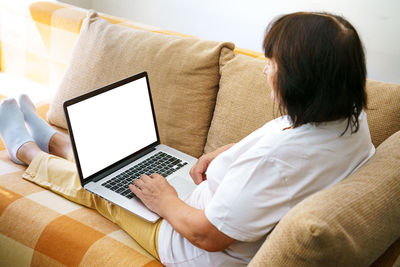 Overjoyed mature woman sitting on sofa in living room talking on video call