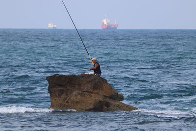 Man fishing in sea against sky