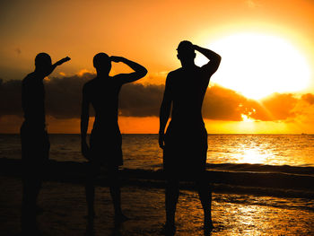 Silhouette friends standing at beach against sky during sunset