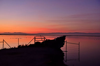 Silhouette railing by sea against orange sky