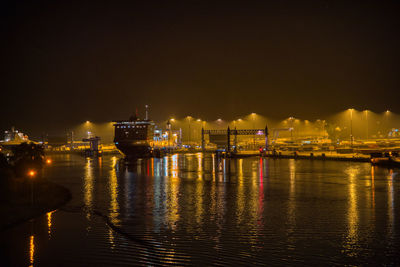 Illuminated buildings by sea against sky at night