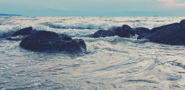 Scenic view of rocks on shore at beach against sky