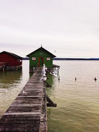 Wooden pier over lake by building against sky