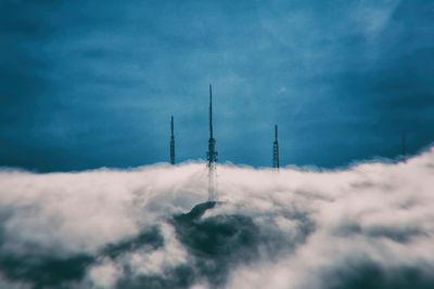 Communication towers covered by clouds against sky