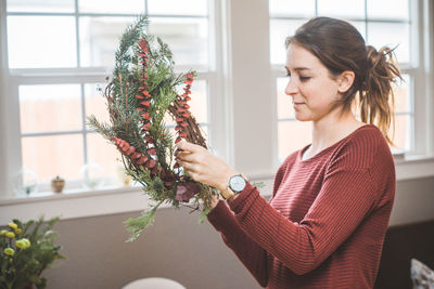 Young woman holding wreath while standing at home