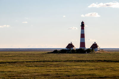 Lighthouse on field by building against sky