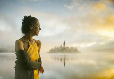 Woman in yellow dress watching a sunrise among the fog on the shores of lake bled, slovenia