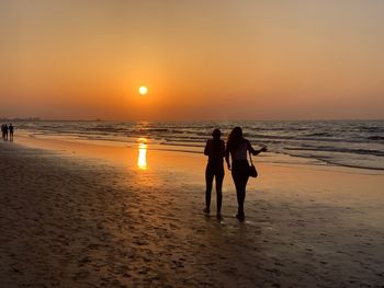 People on beach against sky during sunset