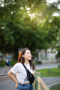 Young woman looking away while standing against trees